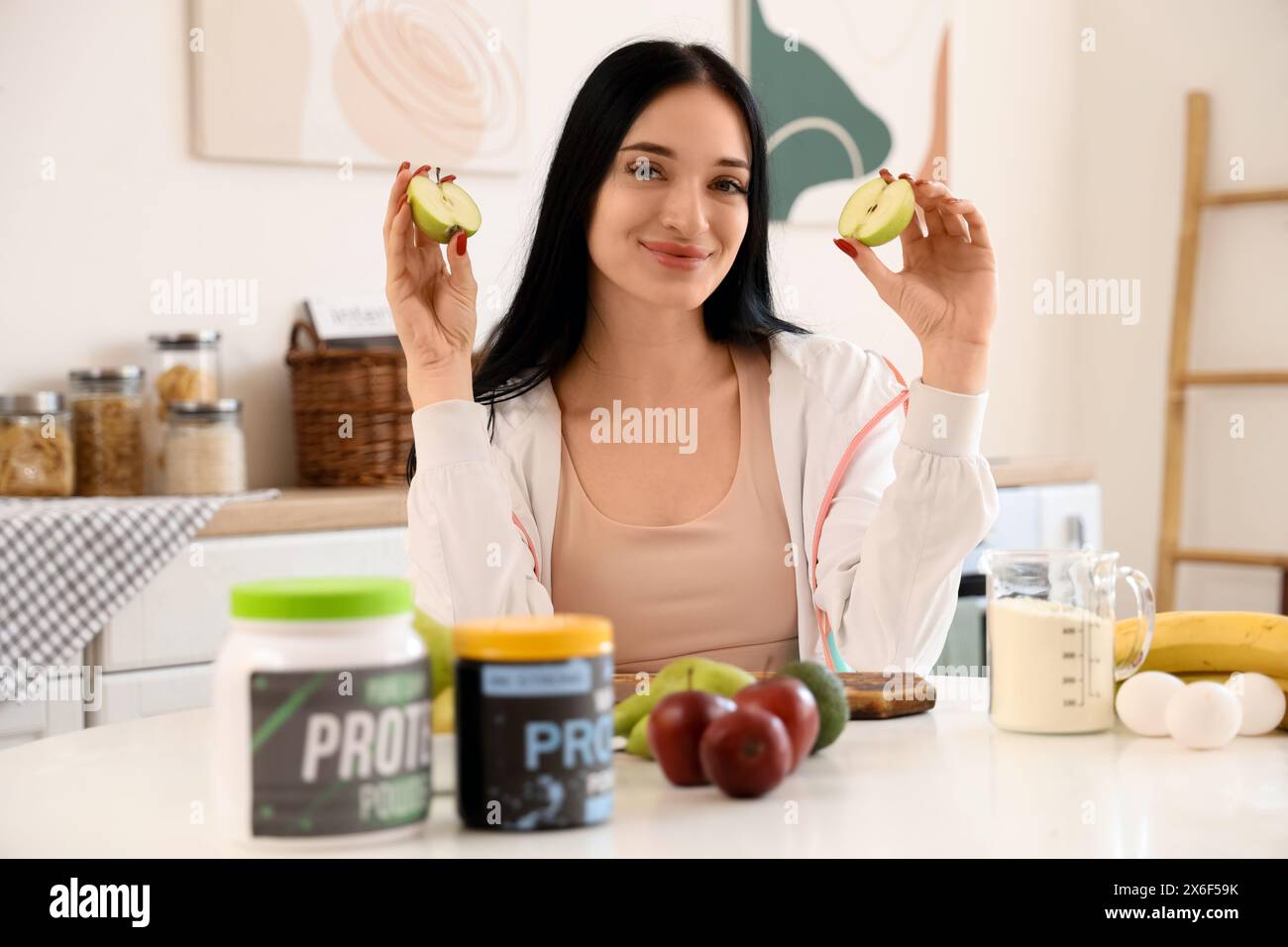 Jeune femme sportive avec pomme coupée faisant shake protéiné dans la cuisine Banque D'Images