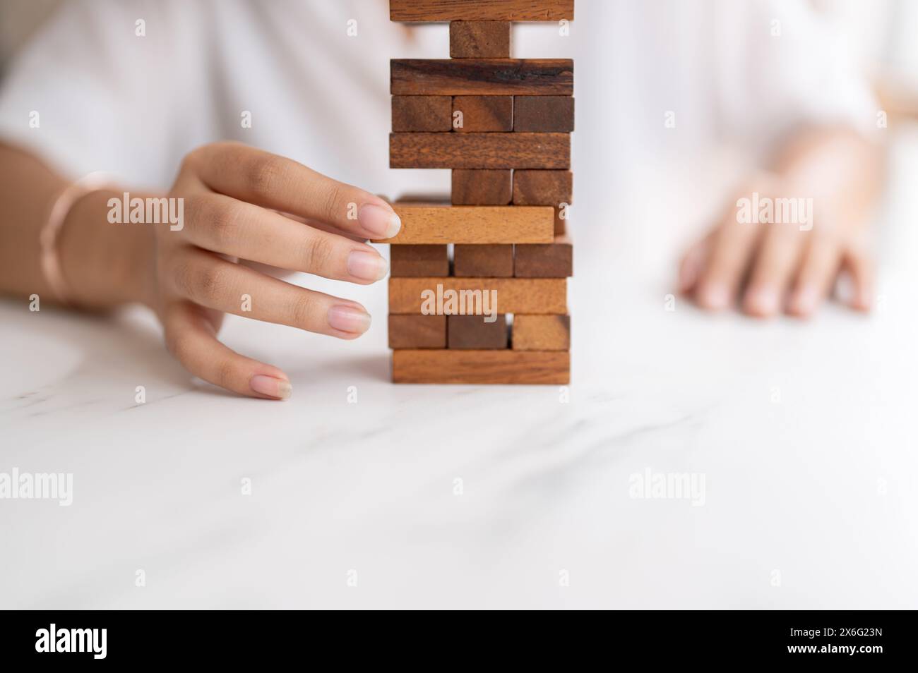 Un gros plan d'une femme prête son attention à jouer à un jeu de blocs de bois à une table, en déplaçant un bloc de bois. jouet, jeu, loisirs Banque D'Images