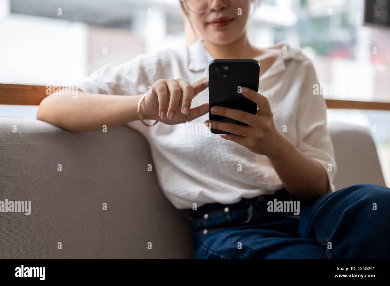 Une image en gros plan d'une femme asiatique vêtue de vêtements décontractés assise sur le canapé dans le salon, utilisant son smartphone pour consulter des messages ou lire un en ligne Banque D'Images