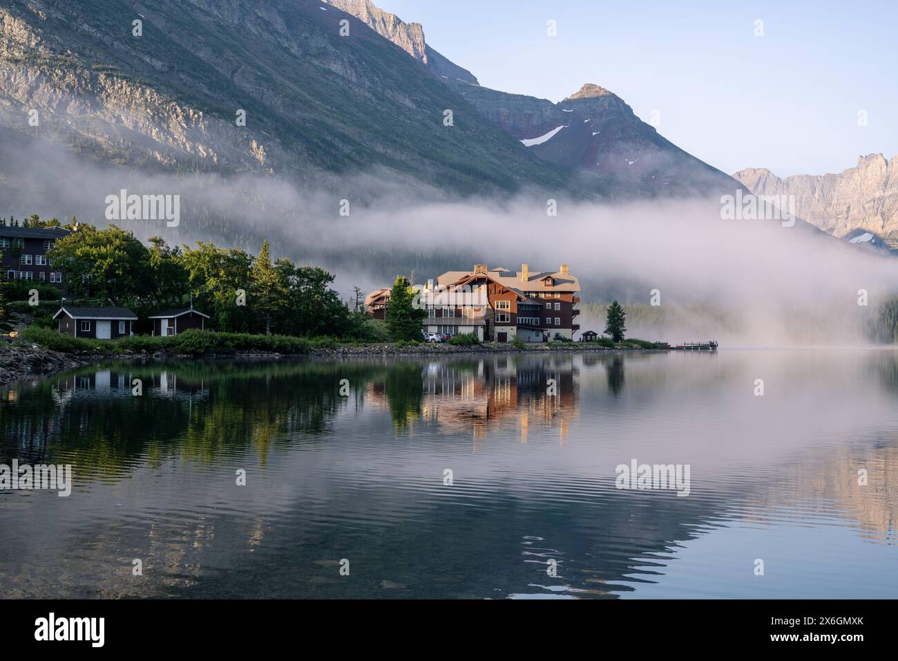 Historique, structure en bois de style ancien sur le bord d'un lac de montagne entouré de brouillard et entouré d'arbres, Many Glacier Hotel, Swiftcurrent Lake, GL Banque D'Images