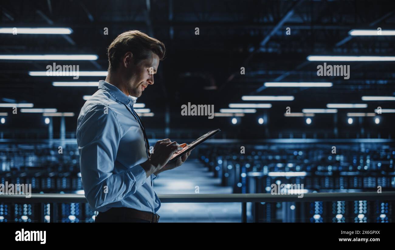 Expert INFORMATIQUE souriant utilisant un ordinateur tablette dans un centre de données. Homme d'affaires prospère et entrepreneur en e-business surplombant l'installation de Cloud Computing de ferme de serveurs. Banque D'Images