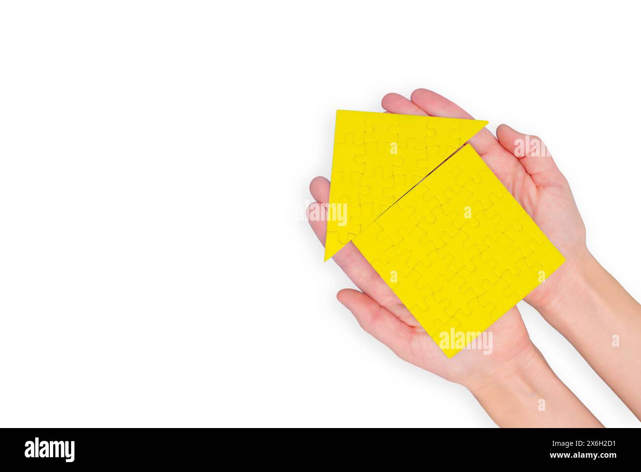 Mains berçant une maison de puzzle jaune sur un fond blanc immaculé. Banque D'Images