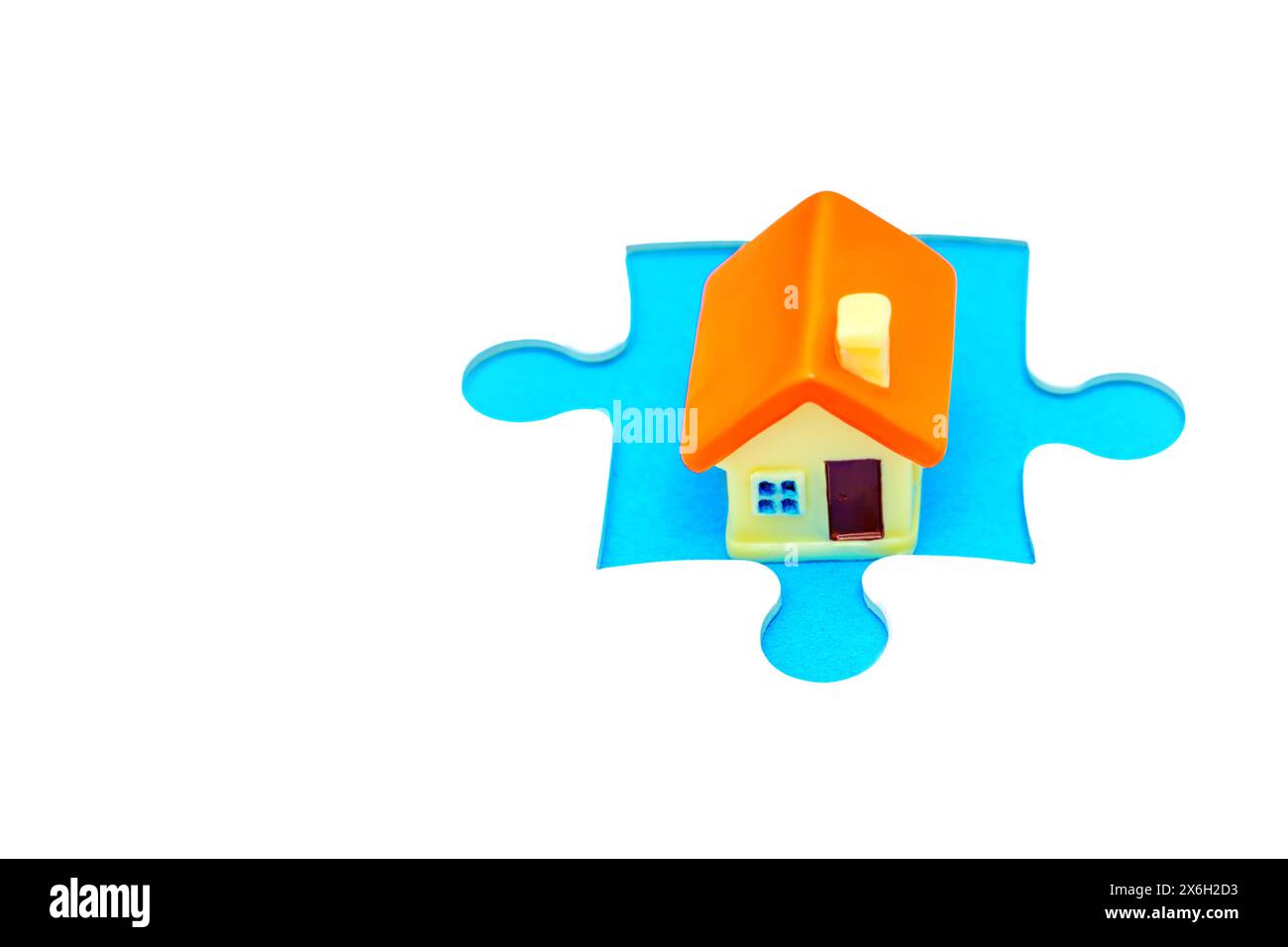 Figurine minuscule maison délicatement placée dans une découpe de pièce de puzzle sur un fond blanc immaculé. Accueil, intégration et interconnexion rel Banque D'Images