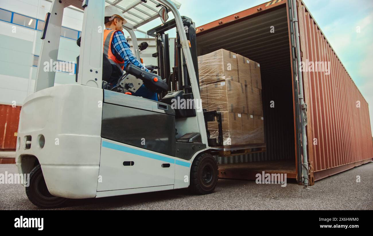 Chauffeur de chariot élévateur chargeant un conteneur de fret d'expédition avec une palette complète avec des boîtes en carton dans le terminal portuaire des opérations logistiques. Banque D'Images