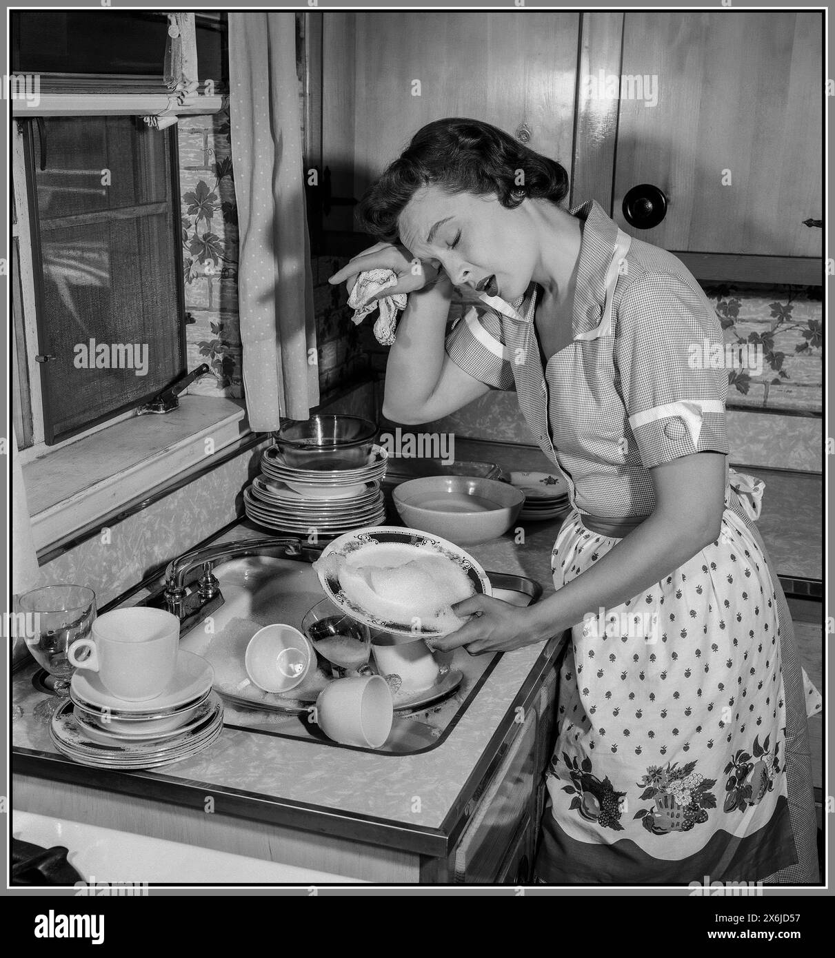 Rétro femme au foyer pose la vaisselle épuisée, mettant sa main sur son front dans une photo promotionnelle exagérée, une femme au foyer et ses tâches domestiques. Amérique États-Unis Banque D'Images