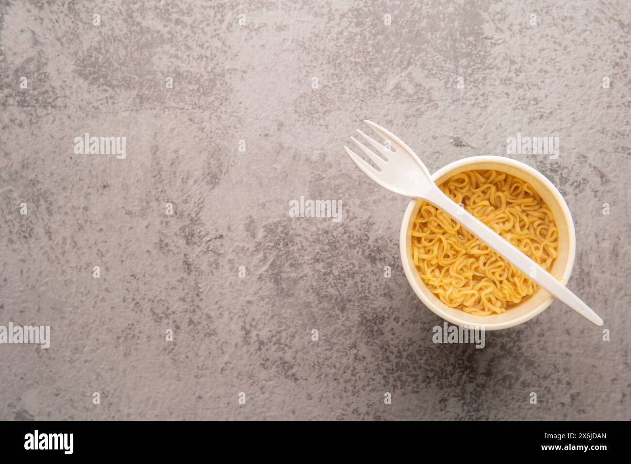 Vue aérienne d'un bol de soupe de pâtes instantanées avec une fourchette en plastique sur un fond gris clair. Déjeuner. Concept de restauration rapide Banque D'Images