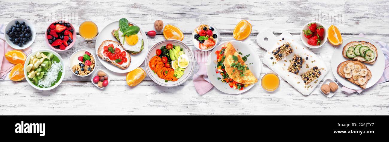 Scène de table saine de nourriture de petit déjeuner. Vue de haut en bas sur un fond de bannière en bois blanc. Omelette, bol nutritif, toasts, barres granola, bol smoothie, Banque D'Images