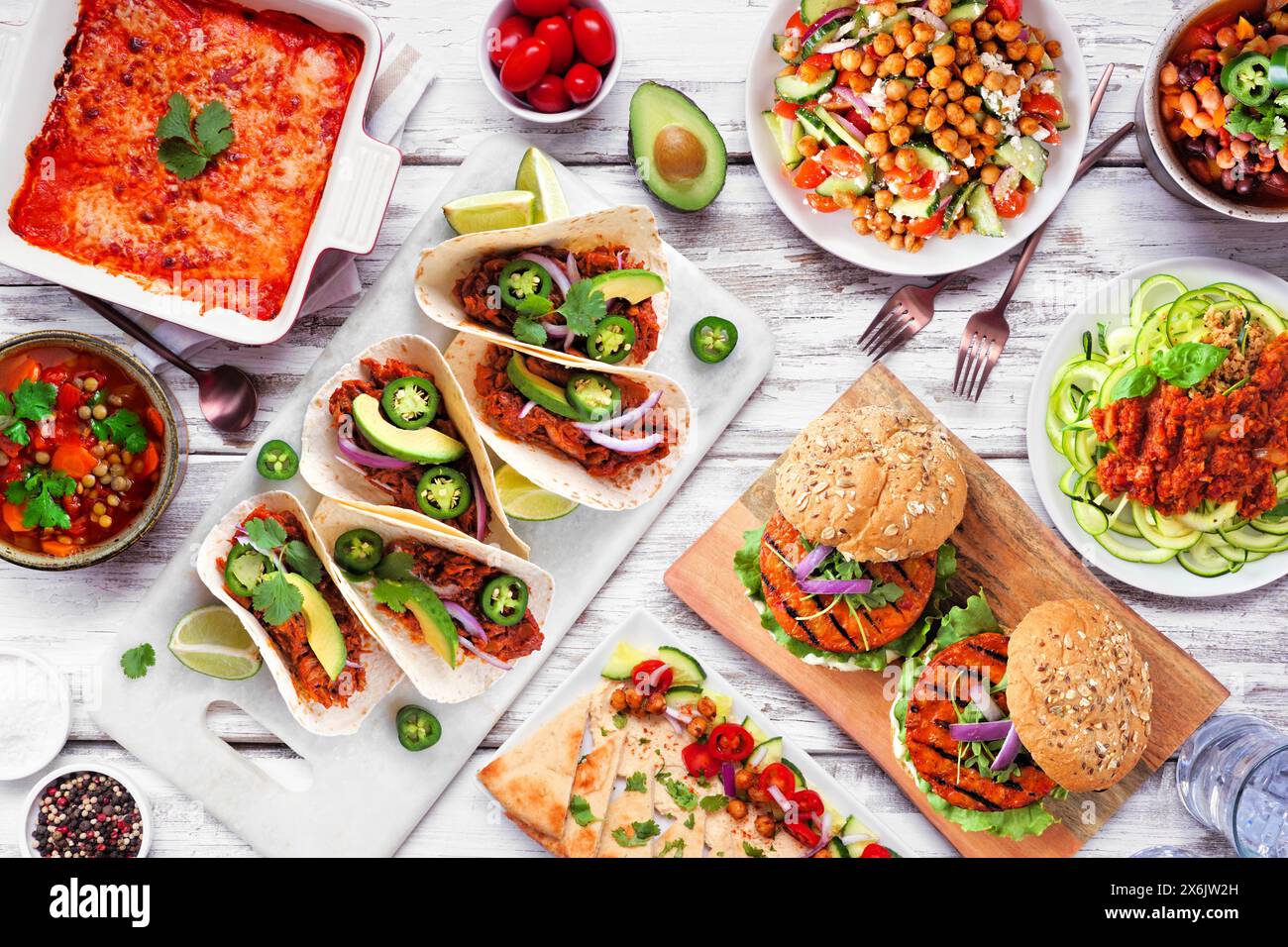 Scène de table de repas végétarienne à base de plantes saines. Vue au-dessus sur un fond de bois blanc. Tacos au jackfruit, lasagnes aux courgettes, zoodles bolognaises aux noix, c Banque D'Images