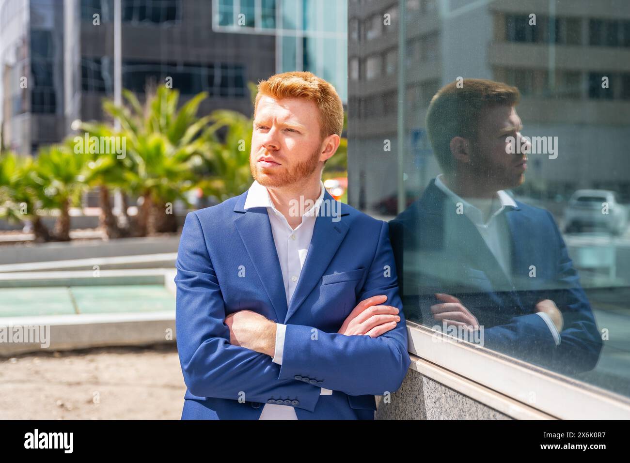 Homme d'affaires fier et pensif debout à côté de la façade en verre d'un bâtiment financier Banque D'Images