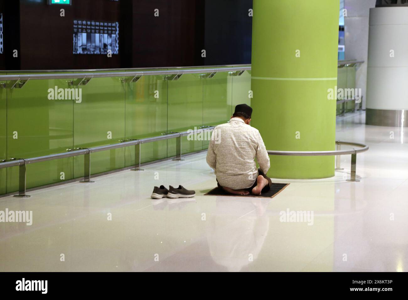 Muslim Man a enlevé ses chaussures et s'est agenouillé sur un tapis de prière priant à l'aéroport international de Muscat Oman Banque D'Images