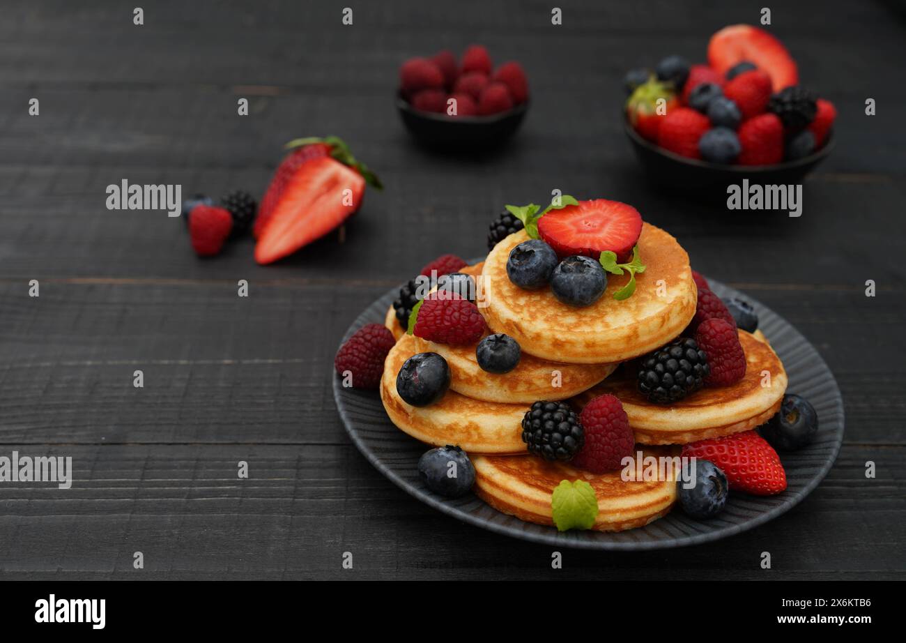 Gros plan de crêpes empilées richement décorées avec différentes baies et feuilles de menthe fraîche sur la surface en bois foncé Banque D'Images