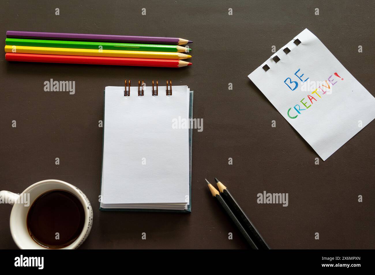 Crayons colorés alignés à côté d'un bloc-notes sur un bureau sombre Banque D'Images