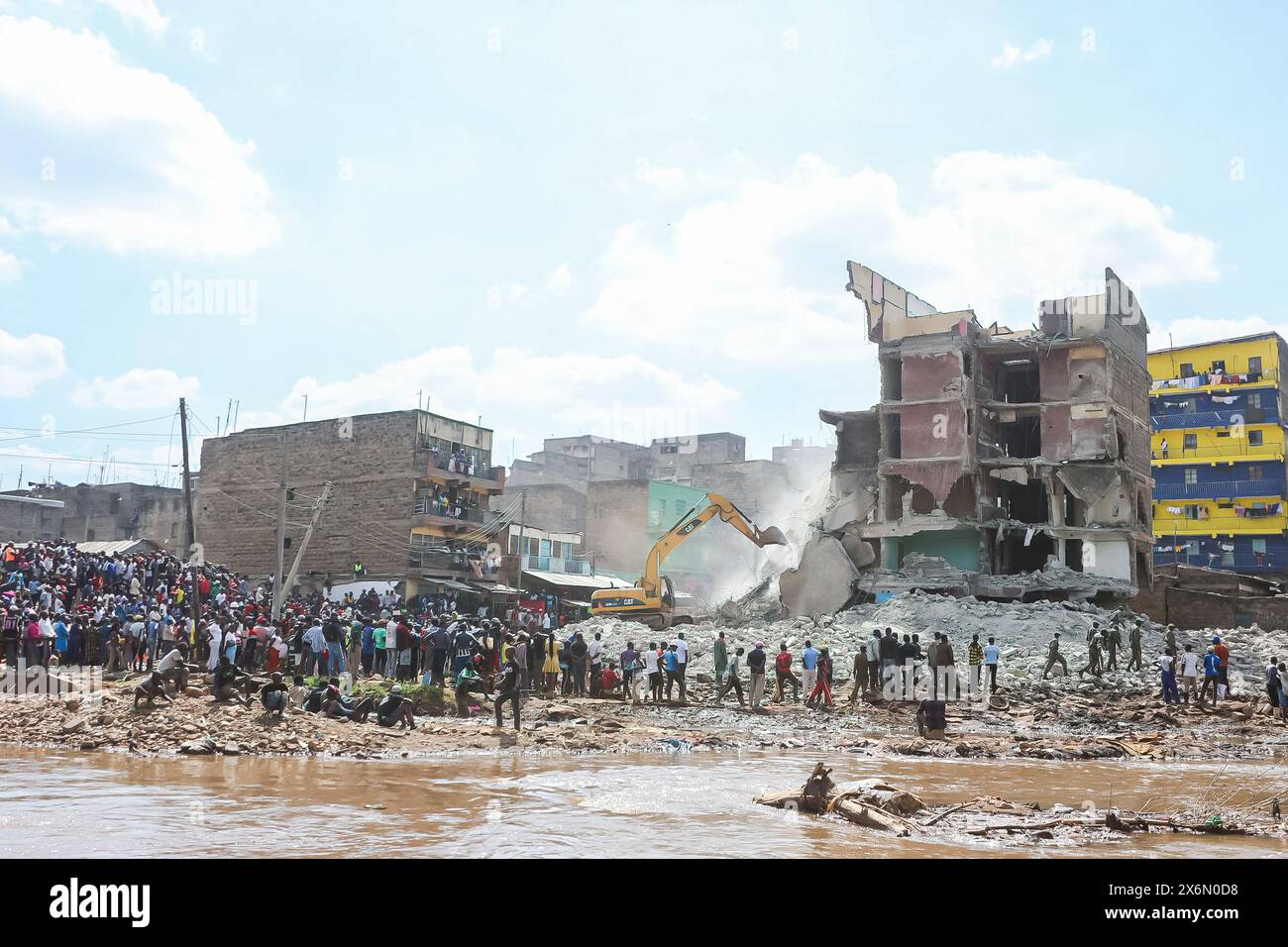 Les habitants se tiennent près de la rivière mathare alors qu'ils regardent un bâtiment est démoli par les multi agences de sécurité kenyanes à Mathare alors que les opérations de sauvetage continuent de libérer les personnes soupçonnées d'être piégées sous les décombres d'un bâtiment effondré le 14 mai 2024. Le gouvernement kenyan a ordonné l’évacuation et la démolition de structures et de bâtiments construits illégalement à moins de 30 mètres des rives du fleuve afin d’éviter des pertes en vies humaines à l’avenir. Les organismes de sécurité continuent de démolir les maisons construites le long des berges autour de Nairobi, qui ont été touchées par les inondations qui ont causé des ravages et ont fait plus de 200 morts jusqu’à présent Banque D'Images