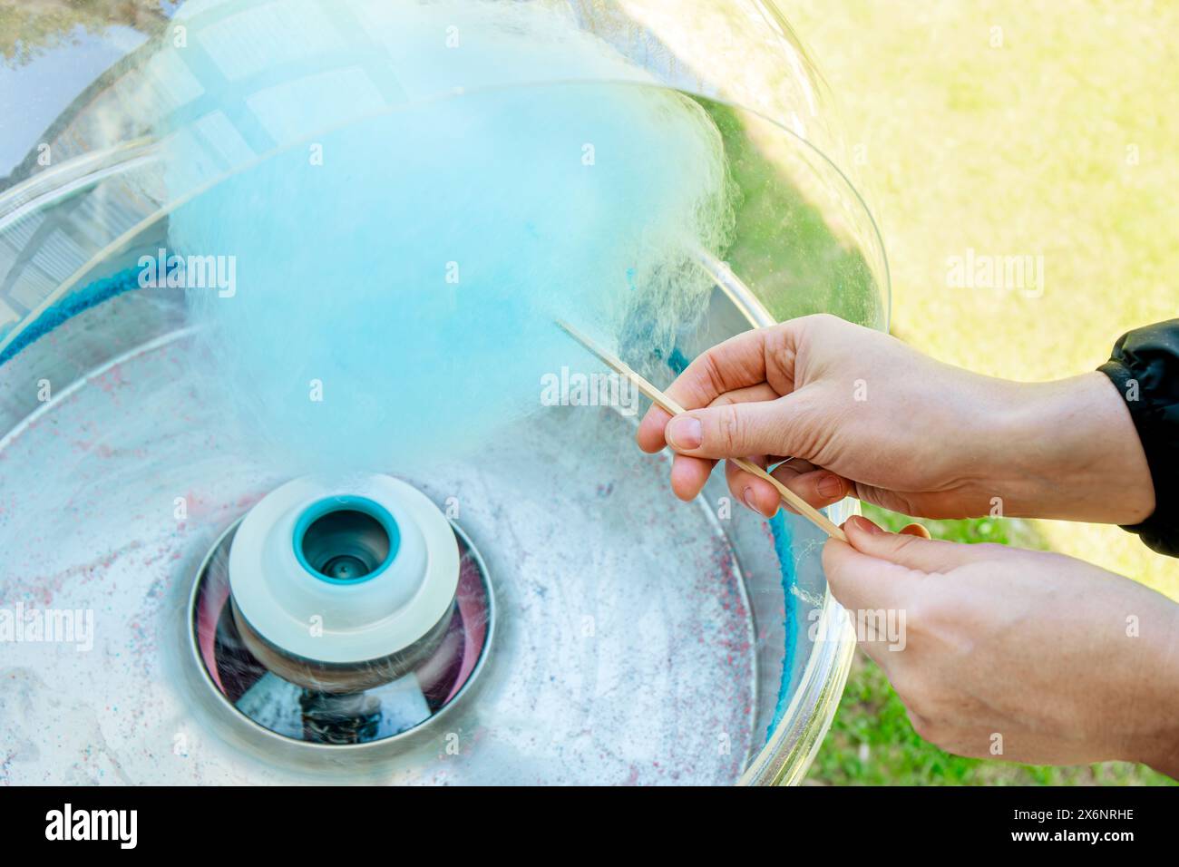 Vue rapprochée des mains de la personne filant la barbe à papa de couleur bleue avec la machine. Tourner autour du bâton de bois. Banque D'Images