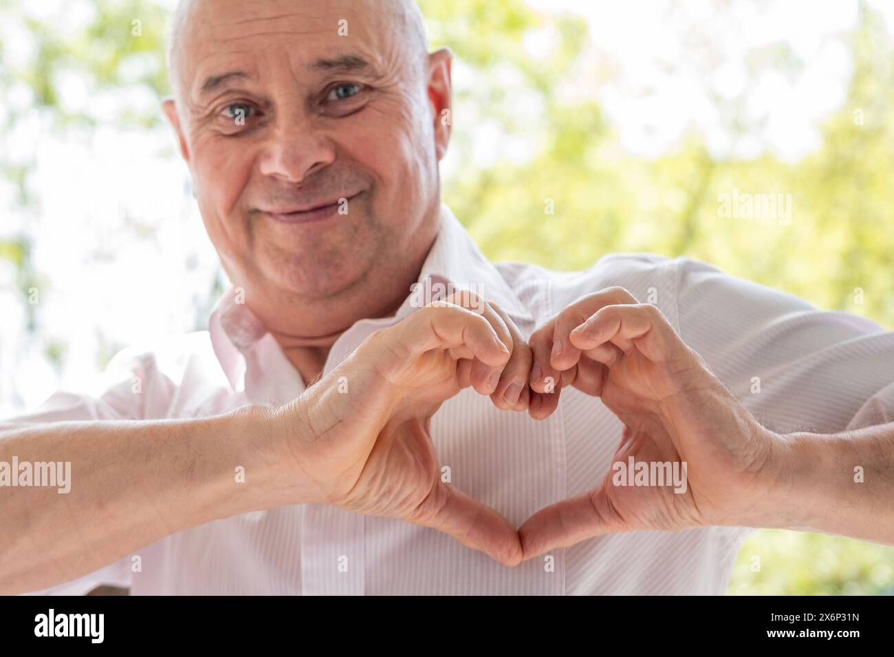 Homme charismatique mature de 65 ans, aîné aimant faisant forme de coeur avec les doigts, la tendresse et les soins, exprimant l'amour et l'affection Banque D'Images