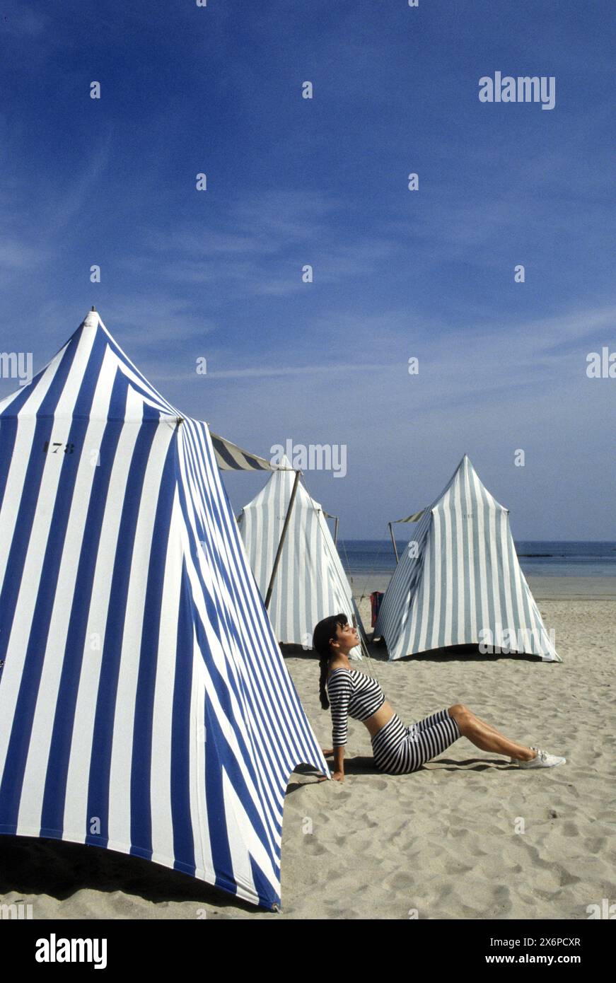 jolie chevelure foncée jeune femme assise sur le sable dans les tentes du milieu sur la plage france bretagne bleu ambiance graphisme Banque D'Images
