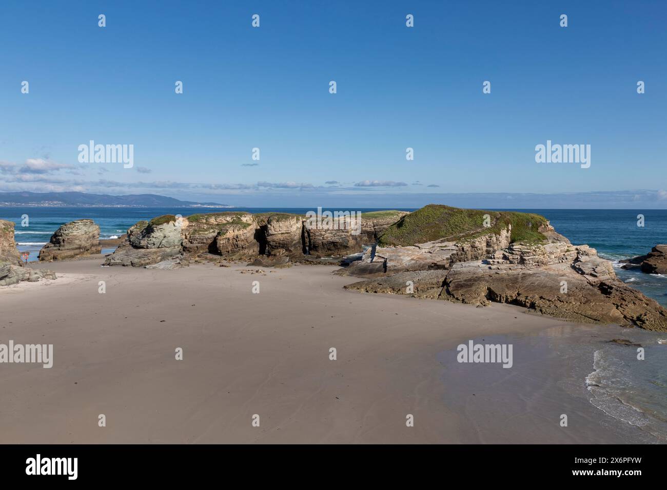 Une plage sereine avec des formations rocheuses, un ciel bleu clair et des eaux calmes, évoquant un sentiment de tranquillité et de beauté naturelle Banque D'Images