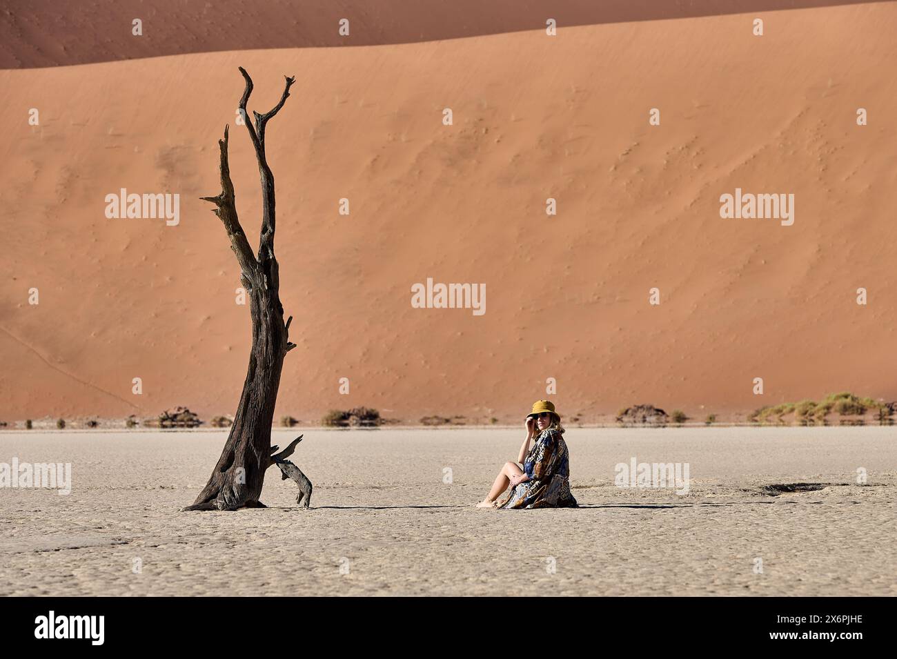 Jeune femme assise à côté de Tree et devant Dune à Deadvlei Banque D'Images