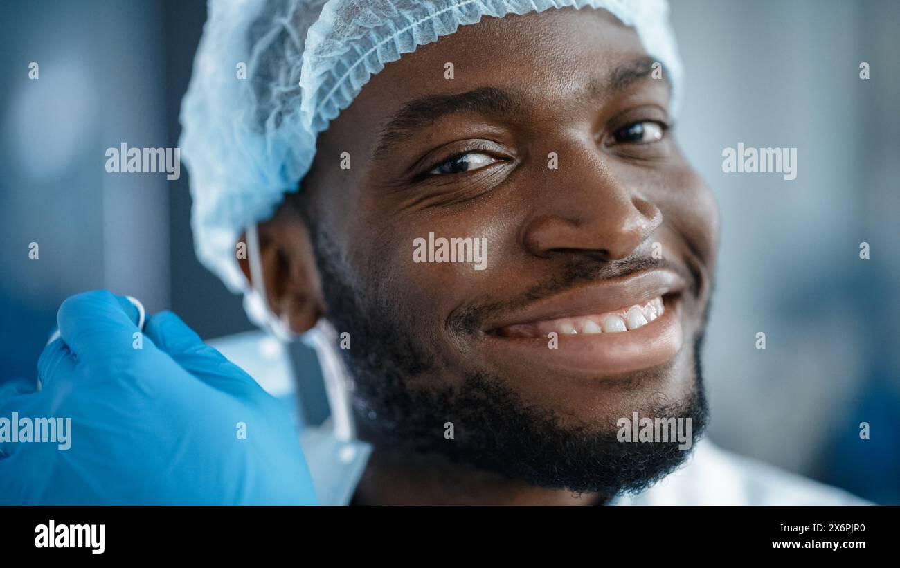 Gros plan Portrait d'un Noir Afro-américain beau homme en chemise blanche décollant un masque facial jetable. Homme réussi regardant calmement la caméra. Homme d'affaires élégant ou un médecin à l'hôpital. Banque D'Images