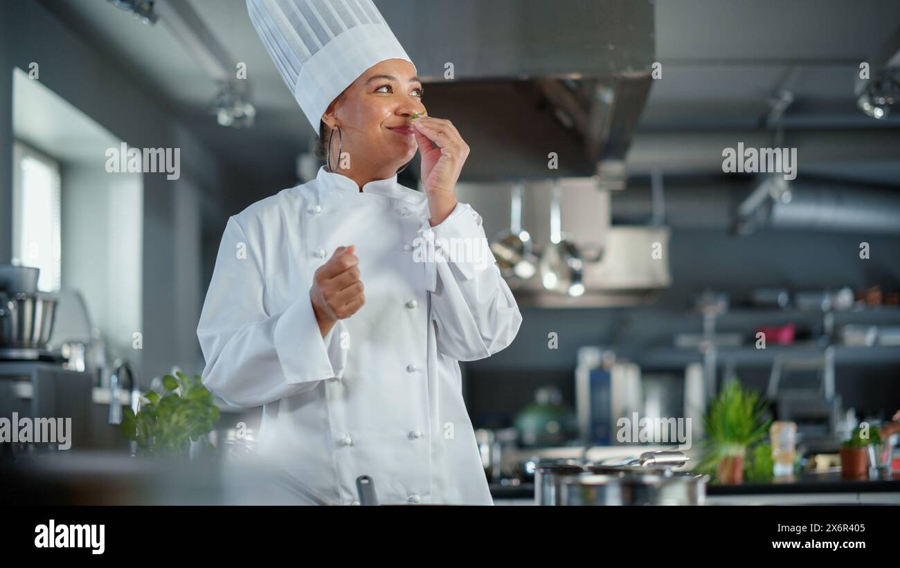 Cuisine du restaurant : Black Female Chef Fries Organic Patty sur une poêle, assaisonne et retourne la côtelette avec un sourire. Cuisine délicieuse et traditionnelle cuisine authentique. Plats gastronomiques sains. Prise de vue moyenne Banque D'Images