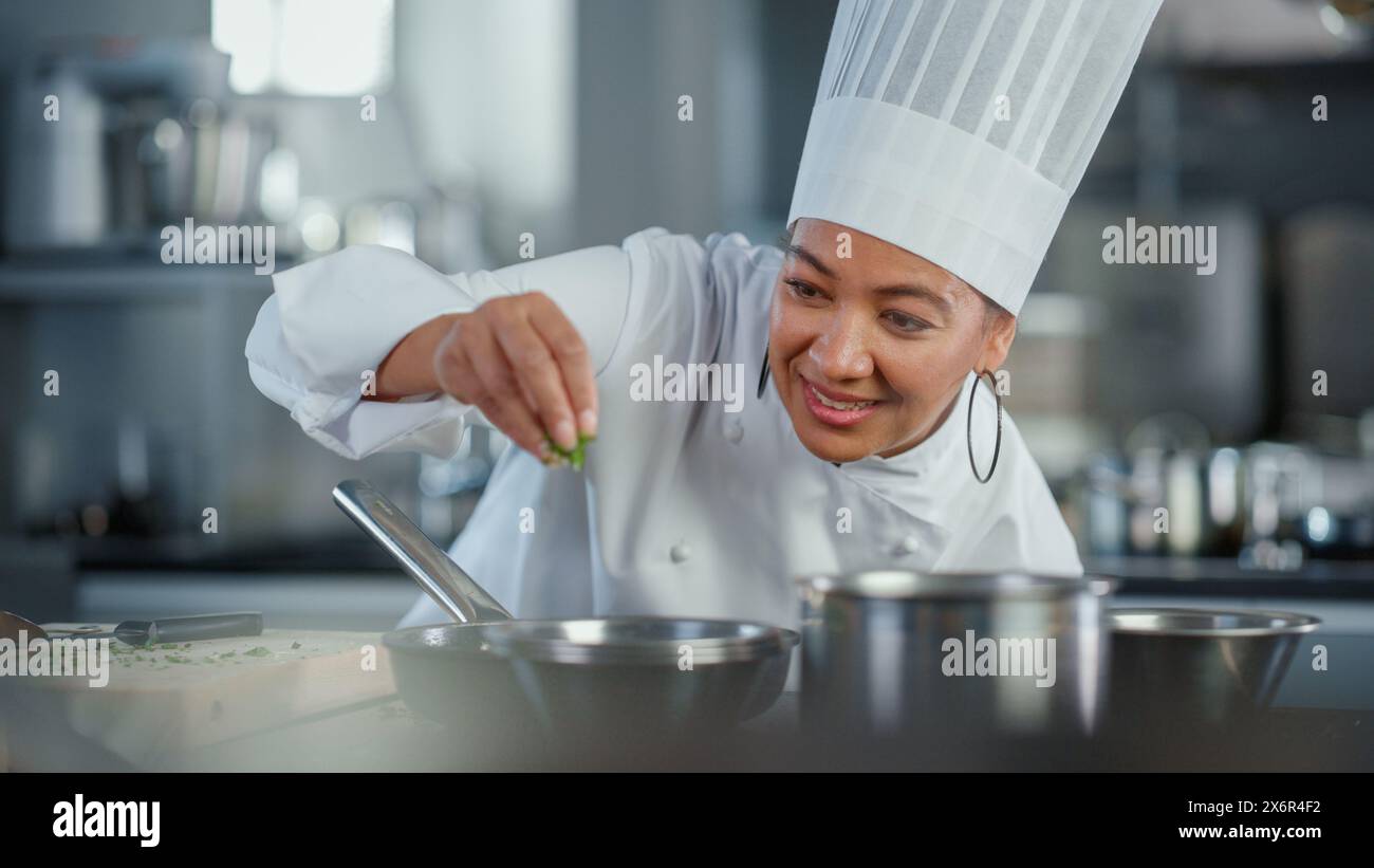 Cuisine du restaurant : Black Female Chef Fries utilise Pan, Seasons plat avec des herbes et des épices, sourires. Cuisine professionnelle cuisine authentique délicieuse et traditionnelle. Des plats sains préparent. Prise de vue moyenne Banque D'Images
