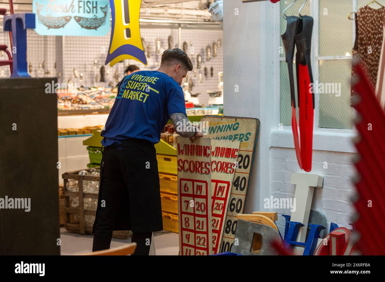 Londres, Royaume-Uni. 16 mai 2024. Un membre du personnel avec des enseignes vintage au supermarché Vintage, un événement pop-up de quatre jours à Soho, par l'équipe de Merchant & Found qui, en tant que «Champions of the Forgotten Maker», ont chargé les principaux fabricants contemporains de créer des œuvres exclusives pour l'événement. Le pop-up fait partie de la London Craft week, un festival organisé dans toute la ville pour célébrer un savoir-faire exceptionnel, dans de multiples secteurs et disciplines. Credit : Stephen Chung / Alamy Live News Banque D'Images