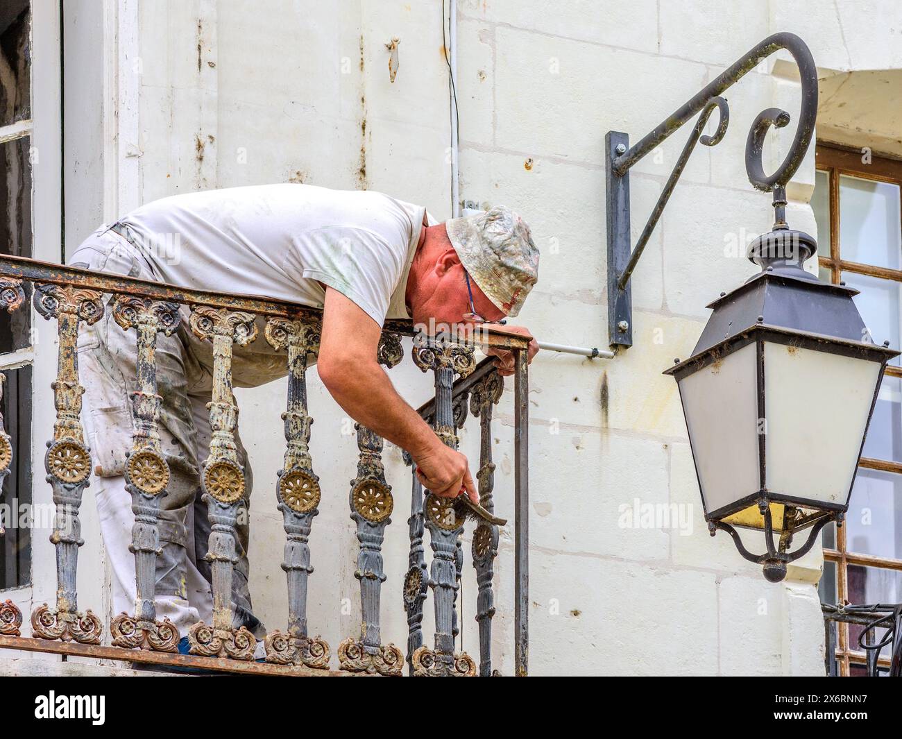 Ouvrier utilisant une brosse métallique pour gratter la peinture et la rouille des balustrades de balcon en fer glacé - Loches, Indre-et-Loire (37), France. Banque D'Images