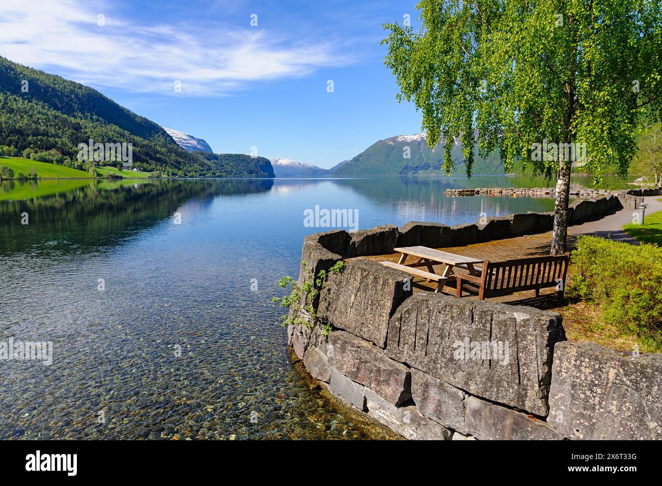 Une vue tranquille sur le lac avec une table de pique-nique en bois sous un arbre luxuriant, situé au milieu de montagnes imposantes et d'eaux cristallines sur un morni de source lumineuse Banque D'Images