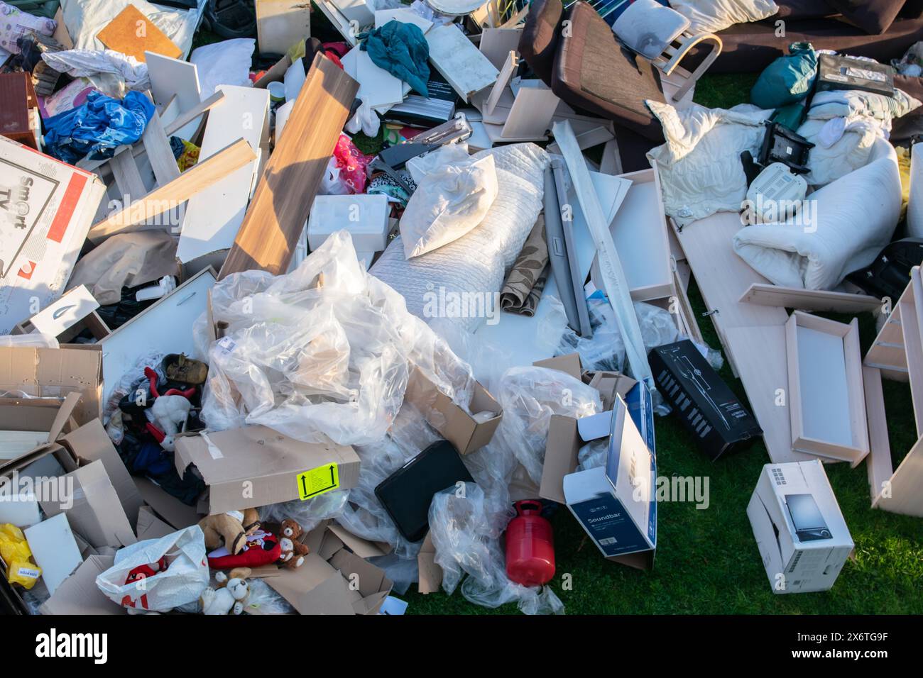 Beaucoup de déchets dans une ville près de la haus. Grandes ordures avec vieux meubles en bois, jouets, boîtes, sacs en plastique dans une rue et l'herbe verte au printemps ensoleillé tra Banque D'Images