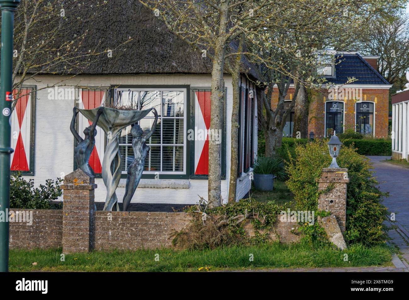 Maison avec de grandes fenêtres et des rideaux rouges, devant elle se dresse une sculpture moderne sous les arbres, maisons anciennes et petites rues avec des lanternes et vertes Banque D'Images