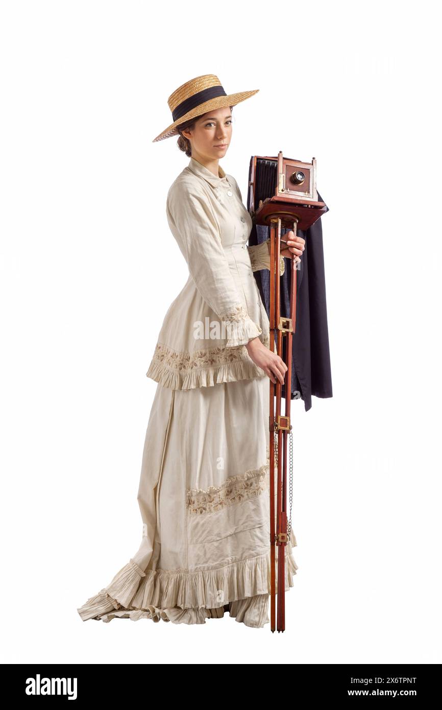 Jeune femme avec appareil photo portant une robe vintage beige des années 1880 et chapeau de paille isolé sur blanc Banque D'Images