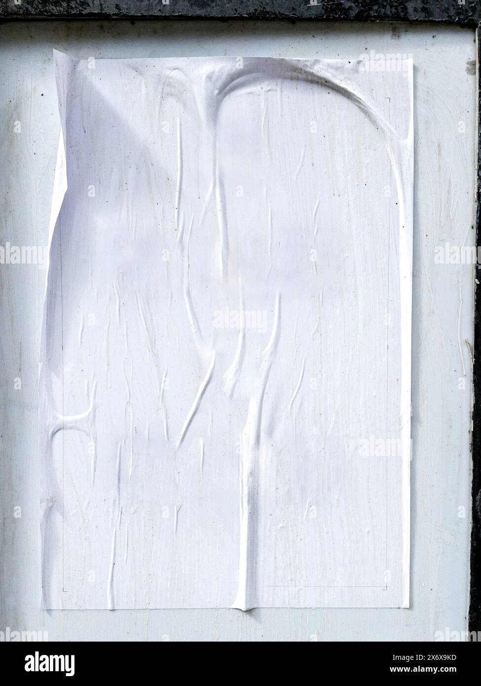 Une affiche blanche froissée collée négligemment sur un mur de pierre, montrant des signes d'usure et d'altération. Banque D'Images