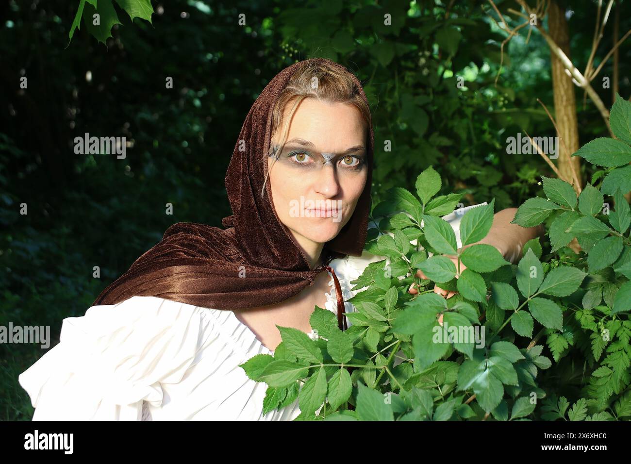 Une femme comme une chasseuse médiévale dans une robe avec une capuche se cache dans la forêt Banque D'Images