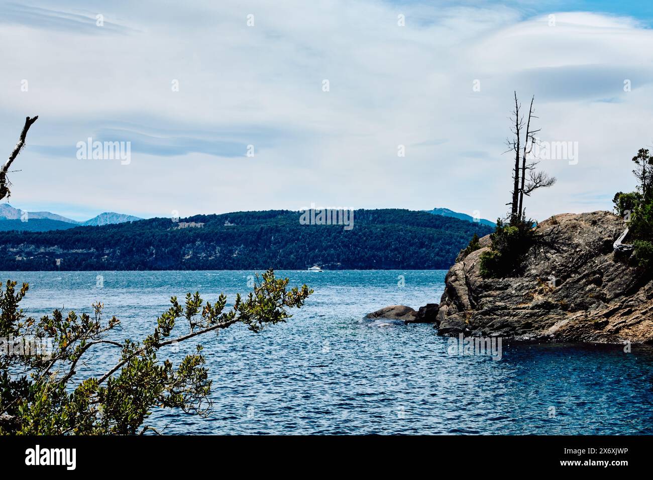 Un lac bleu avec un yacht visible au loin sur fond de montagnes rocheuses couvertes d'arbres, Parc National de Bariloche Banque D'Images