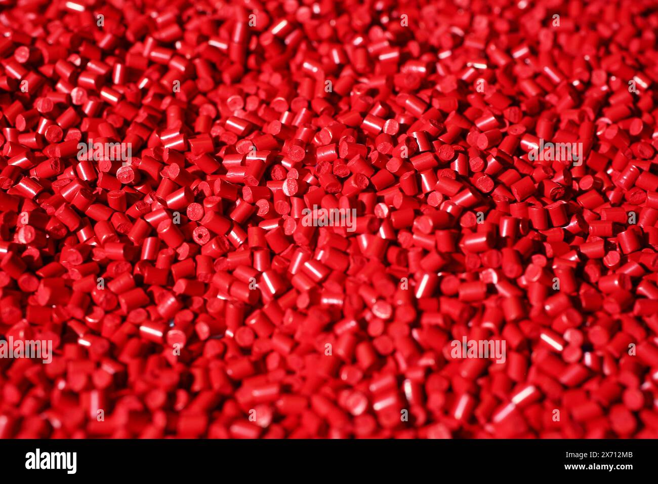 Cadre macro de granulés de plastique rouge. Le composite polymère est versé dans un réservoir pour la production ultérieure et le coulage dans des moules spéciaux. Banque D'Images