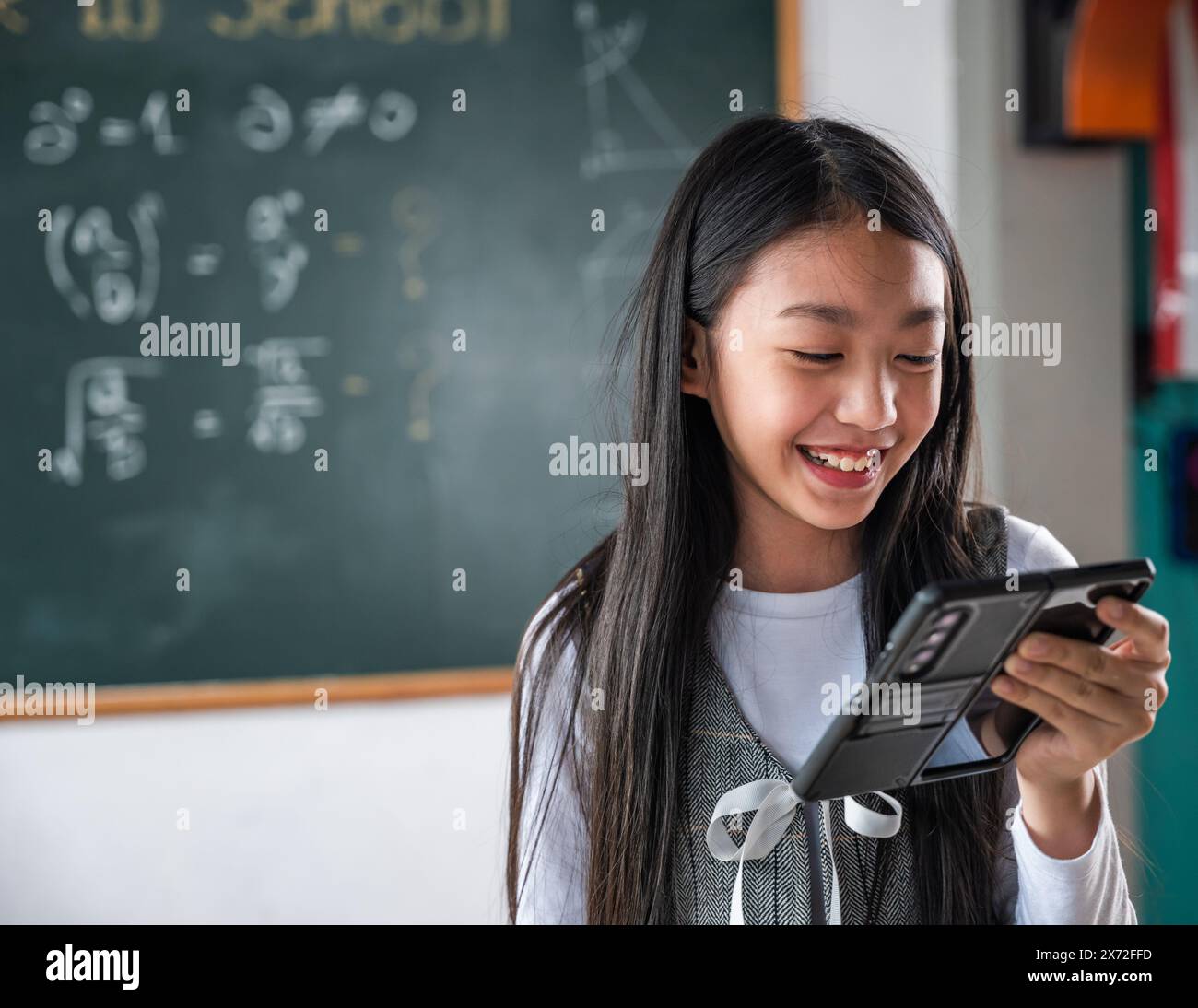 Une fille sourit tout en tenant un téléphone portable devant un tableau noir avec des maths Banque D'Images