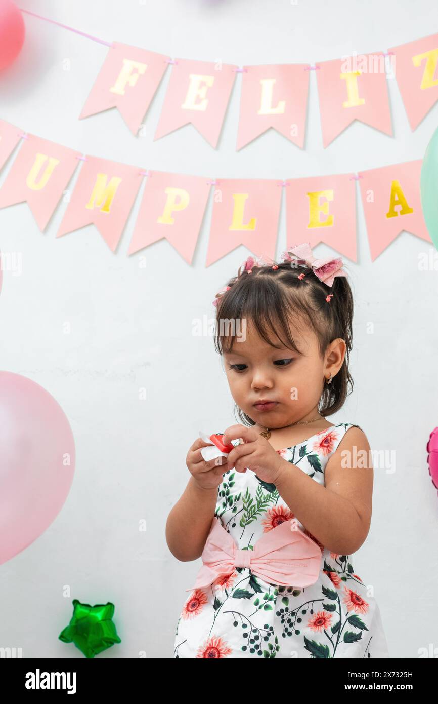 petite fille brune latina essayant d'ouvrir l'embolture d'un bonbon, signe joyeux anniversaire en espagnol Banque D'Images