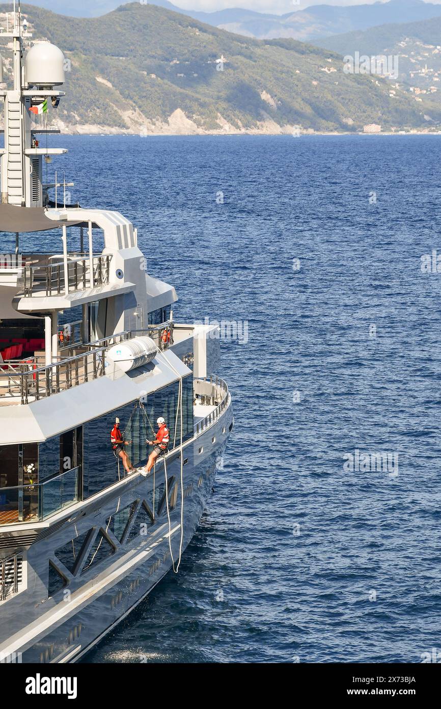 Membre d'équipage d'un méga yacht de luxe ancré dans la baie de Cannon lavant les fenêtres extérieures attelées aux cordes Portofino, Gênes, Ligurie, Italie Banque D'Images