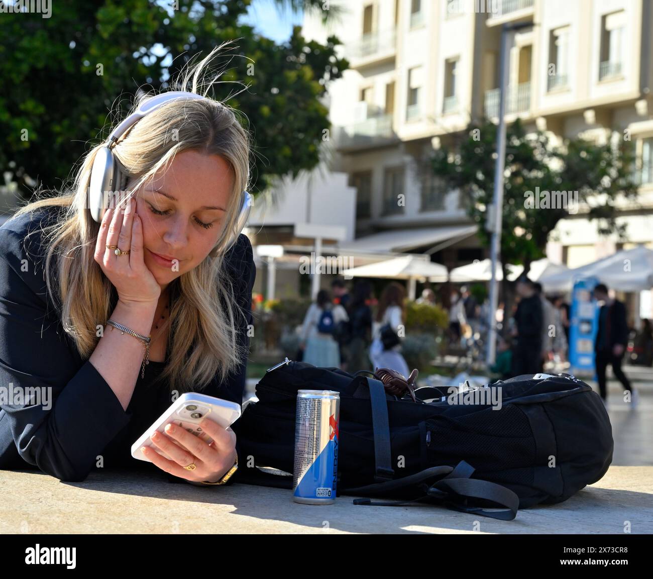 Jeune femme blonde attrayante regardant un téléphone intelligent écoutant de la musique sur des écouteurs sur fond de ville Banque D'Images