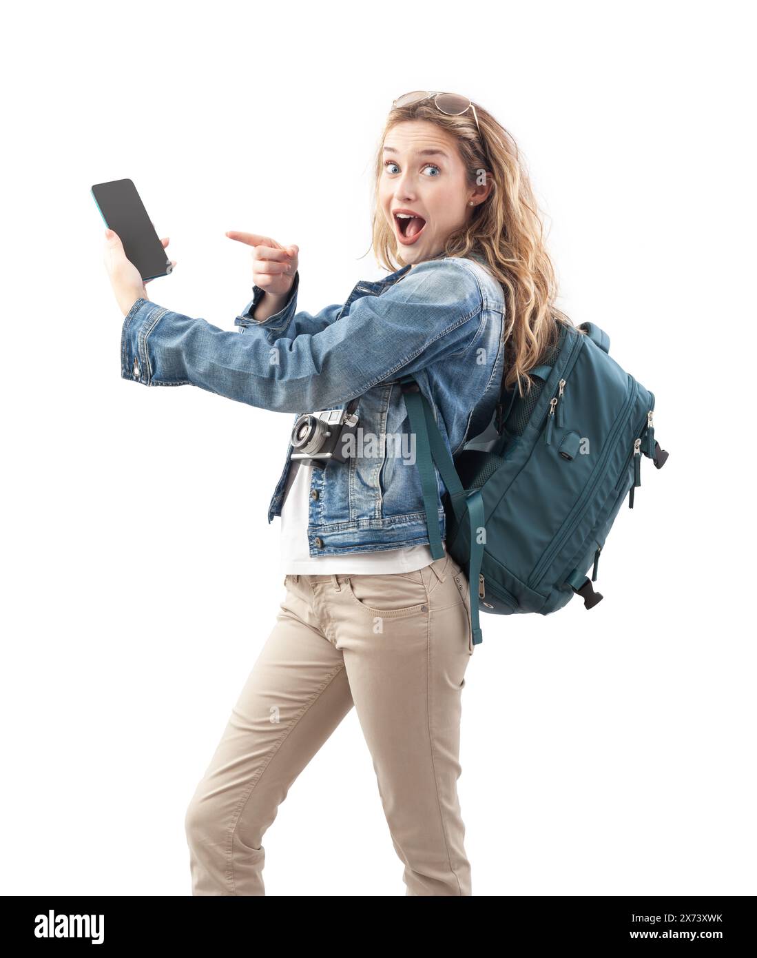 Jeune voyageuse touristique excitée pointant vers l'écran de son smartphone, portant un sac à dos sur ses épaules, isolée sur un fond blanc. Co Banque D'Images