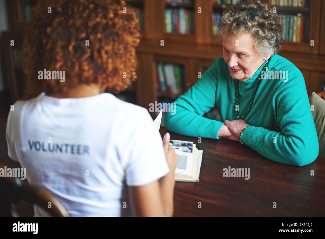 Livre, lecture et femme aînée avec bénévole dans une maison de retraite pour le service communautaire, la responsabilité sociale ou la sensibilisation. ONG, personne âgée avec Banque D'Images