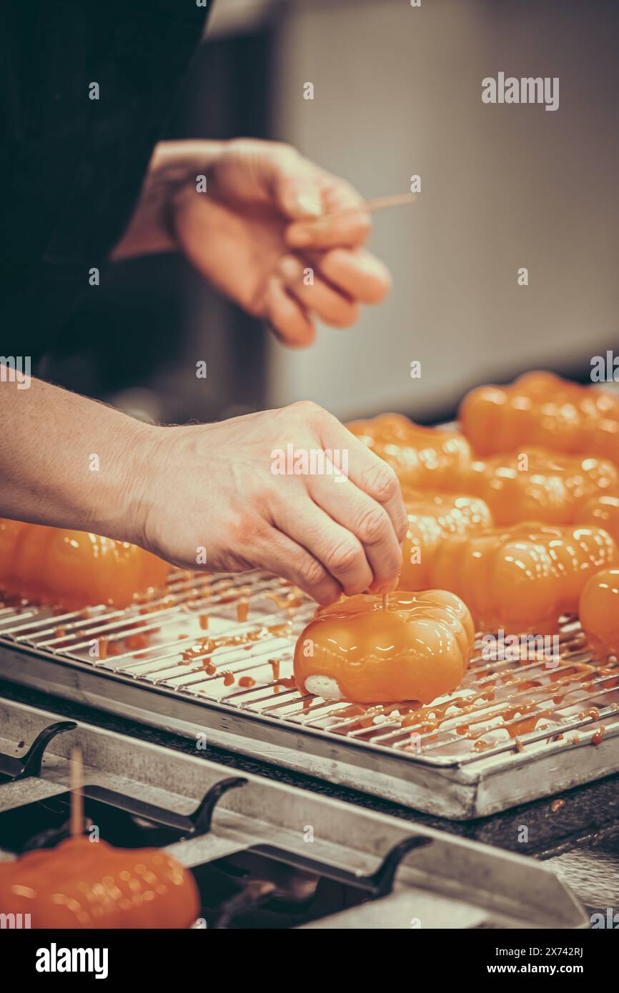 Mains de la confiseuse femelle décorant des tartes glacées orange. Préparation des tartelettes par un pâtissier professionnel. Vertical. Banque D'Images