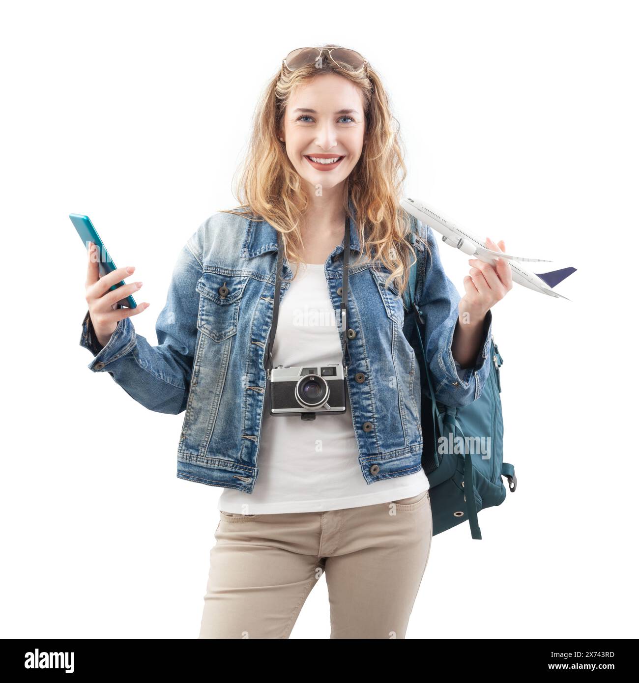 Heureuse jeune femme voyageuse touristique montrant l'écran de smartphone et un modèle d'avion, portant sac à dos sur les épaules, isolé sur fond blanc Banque D'Images