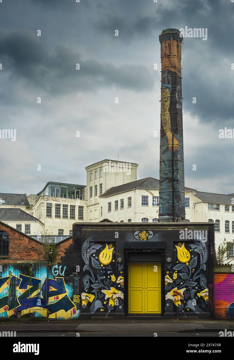 Digbeth Custard Factory. Scène de l'ancienne usine industrielle avec cheminée en briques haute et mur de premier plan avec graffiti coloré et porte jaune Banque D'Images