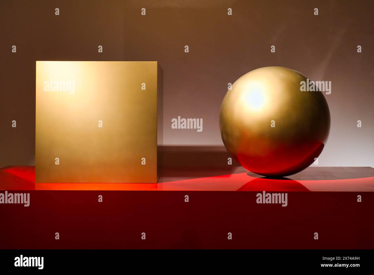 Vue d'un cube doré et d'une sphère sur une table rouge Banque D'Images