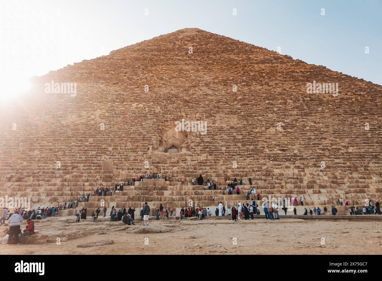 Les touristes se rassemblent à la base de la Grande Pyramide de Gizeh, en Egypte, grimpant ses marches de pierre massives sous le soleil Banque D'Images