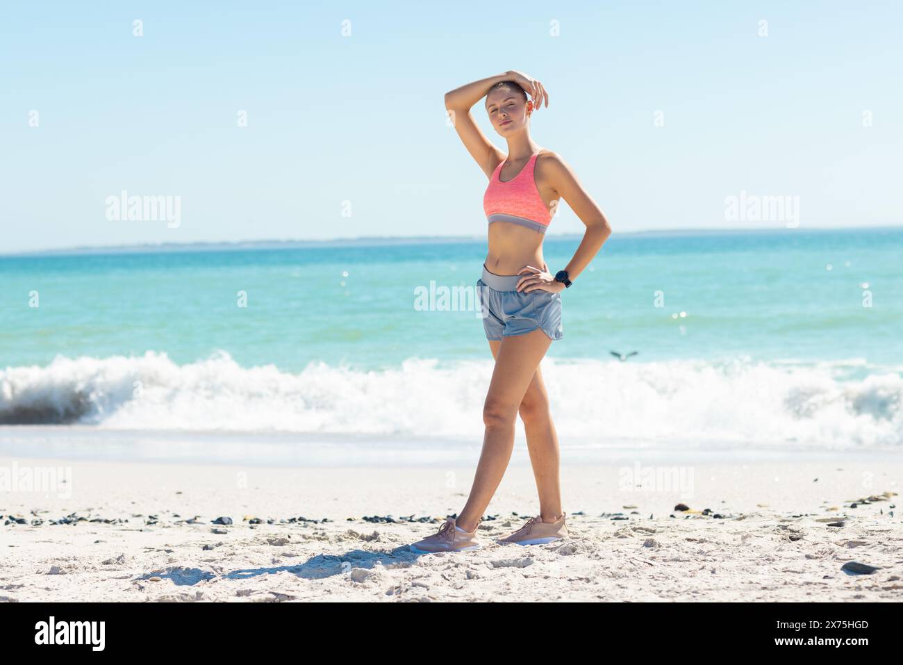 À la plage, jeune femme caucasienne debout, main sur la tête, regardant loin Banque D'Images