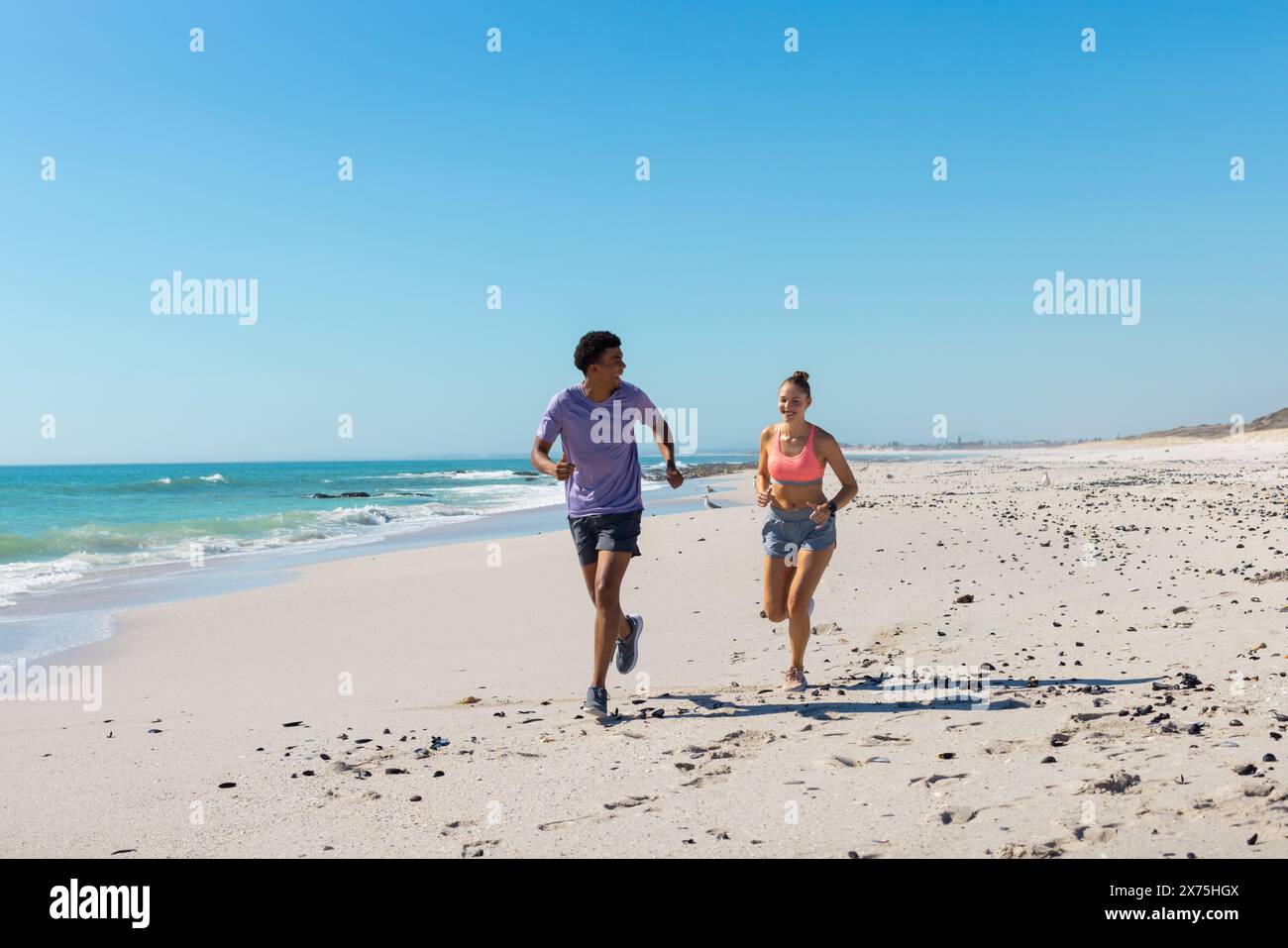 À la plage, couple diversifié portant des vêtements d'été, courant sur la plage ensoleillée Banque D'Images