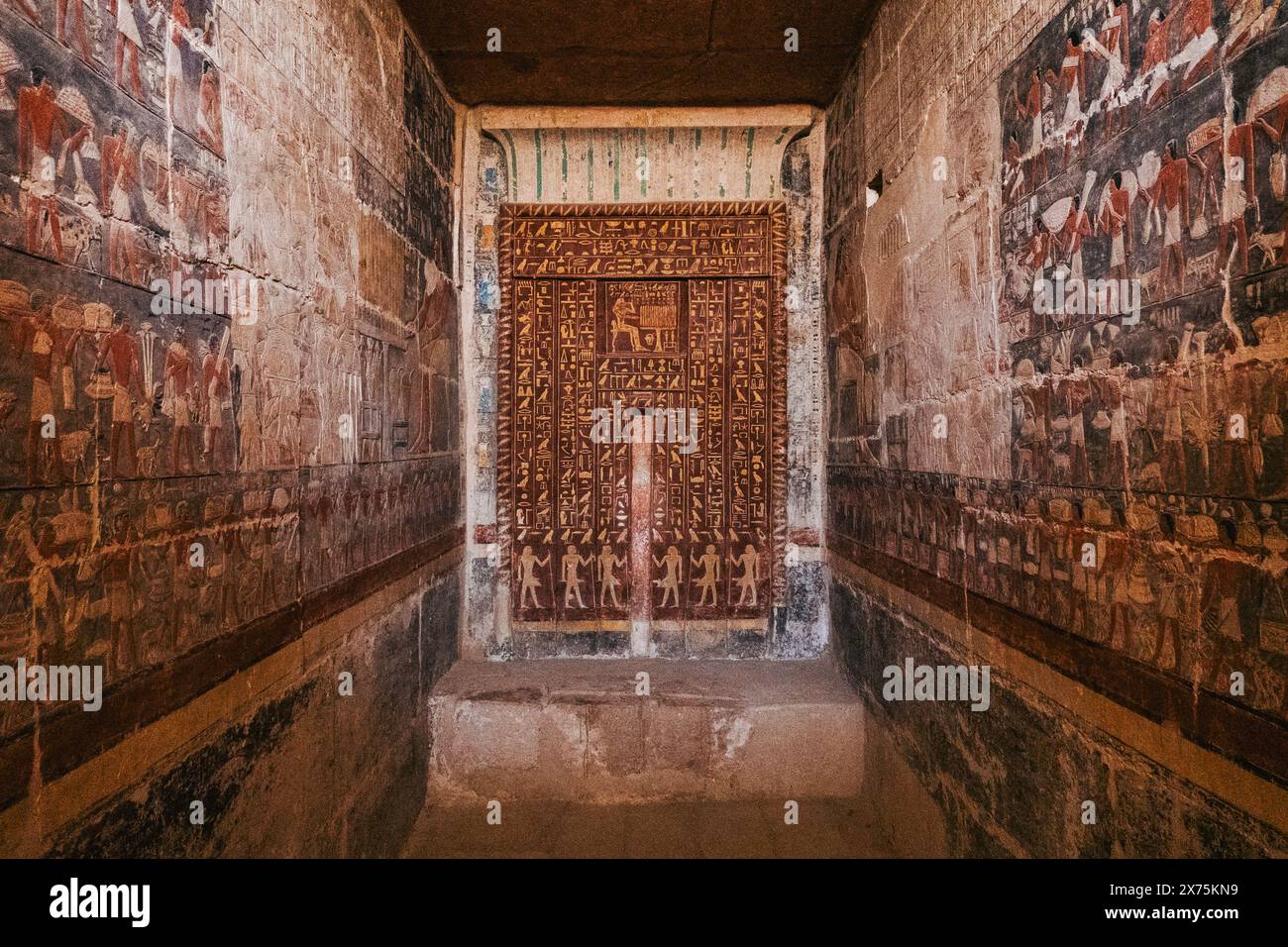 Chambre hautement décorée dans un tombeau de Saqqara avec une fausse porte et des reliefs peints vibrants de figures, offrandes et rituels de l'ancien Empire. Banque D'Images
