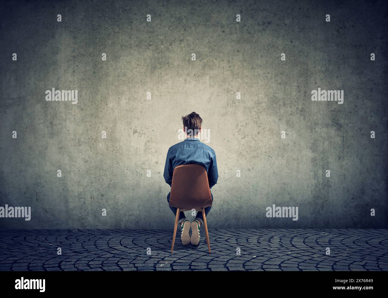 Un jeune homme est assis sur une chaise et regarde un mur de béton vide Banque D'Images